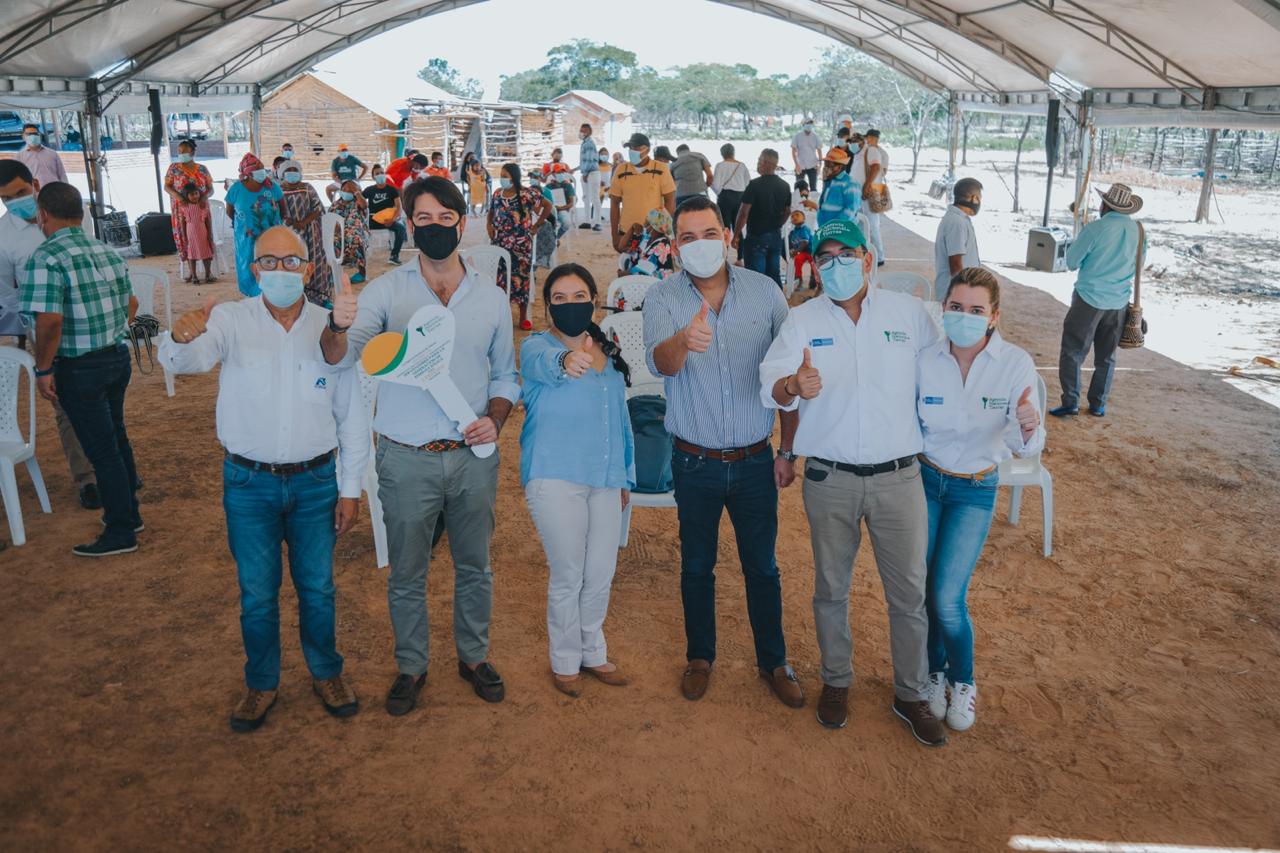 La Directora de la ANT, Myriam Martínez Cárdenas,  en compañía de cuatro funcionarios de la ANT y de un beneficiario de títulos posan en alineados, cada uno con su brazo levantado y pulgar arriba. De fondo varios integrantes de un resguardo de la comunidad Wayúu. 