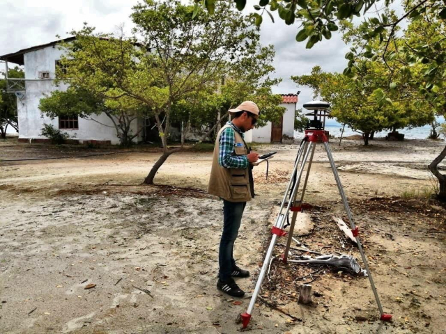 Hombre topógrafo, funcionario de la ANT, en trabajo en campo en terreno de Arroyo Grande en Cartagena levantando información.