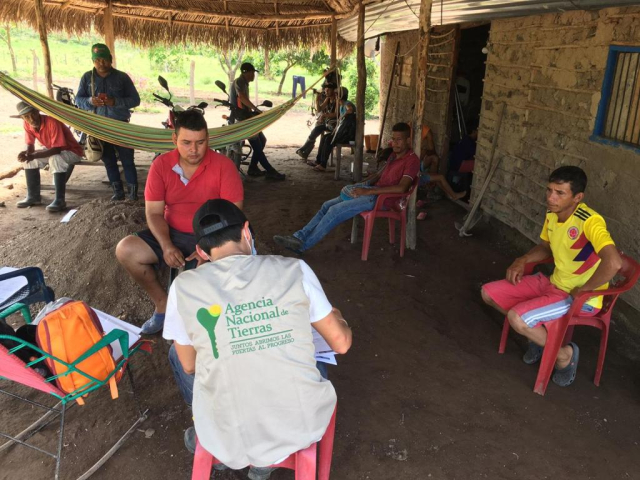 Se ve a una funcionaria de la ANT, sentada en silla de plástico mientras conversa y toma datos de los campesinos, principalmente a tres de ellos. Aproximadamente habla principalmente