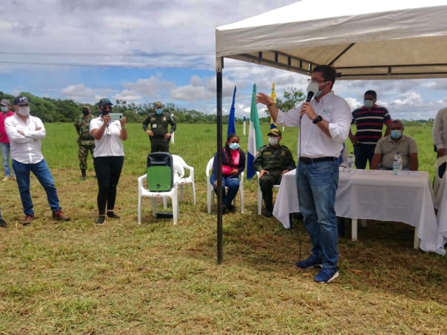 Funcionario de la ANT, vestido de camisa blanca, pantalón azul y tapabocas, en compañía de dos hombres policías, uno del ejercito y algunos campesinos, ubicados en una carpa instalada con una mesa cubierta por un mantel blanco, hacen oficial la entrega del predio La Esperanza en San José del Guaviare.