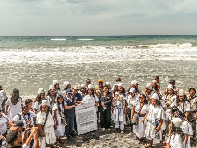 un-grupo-de-personas-paradas-en-la-playa-con-un-cartel