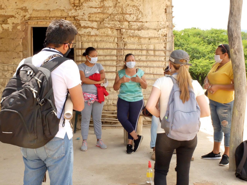 Dos funcionarios de la ANT quienes están de espalda, hablan con cuatros mujeres campesinas de Fonseca, la Guajira, y de fondo una casa de una ranchería.