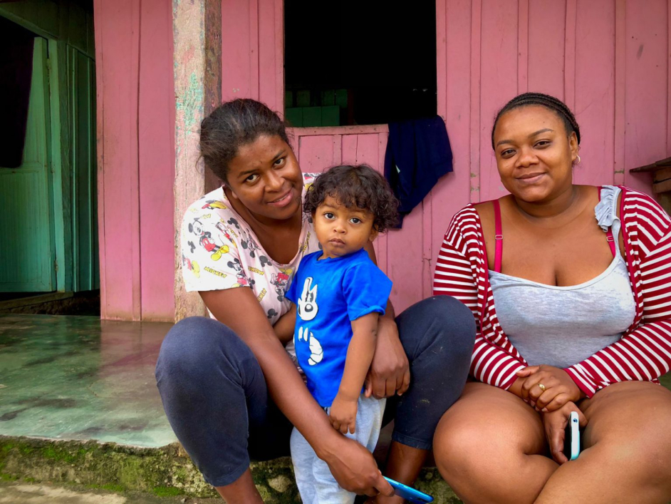 Dos mujeres y un niño pequeño, sentados afuera de su casa.