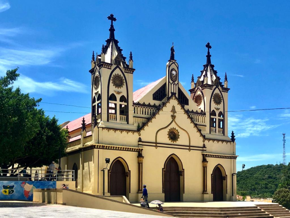 Iglesia del Parque principal Ovejas, Sucre. Esta es de color amarillo con bordes cafés. De fondo el cielo azul y a los costados verdes árboles.