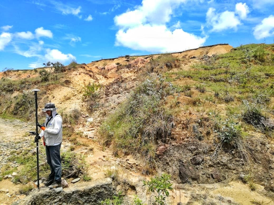 Hombre sobre montaña de color amarillo y algunas partes con pasto verde y cielo azul con nubes blancas.